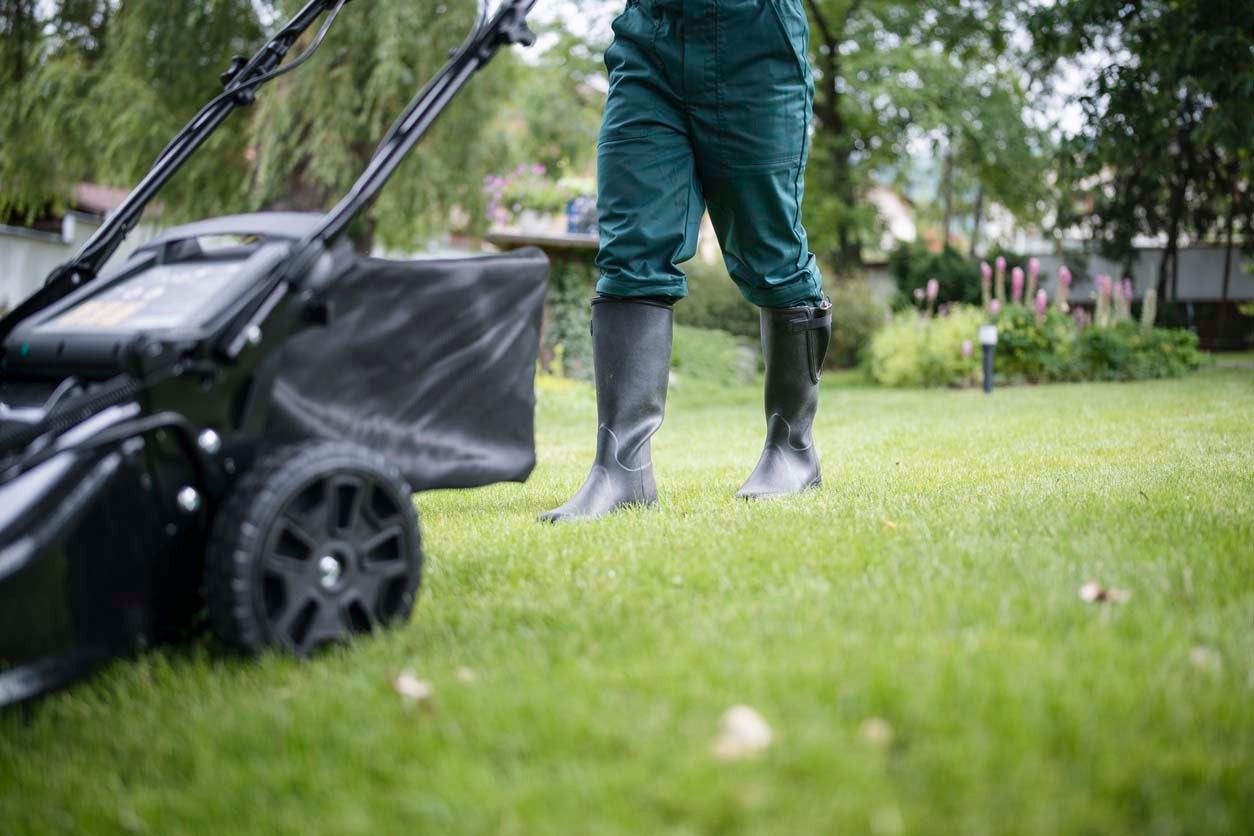 A close up of a person mowing a lawn with a push mower for a do it yourself lawn care program.